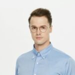 Professional portrait of a man wearing glasses and a blue shirt, isolated on white background.